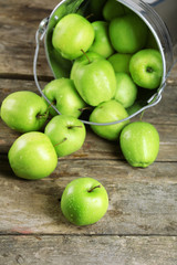 Ripe green apple in metal bucket on wooden table close up