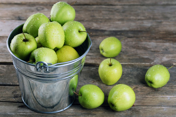 Ripe green apple in metal bucket on wooden table close up