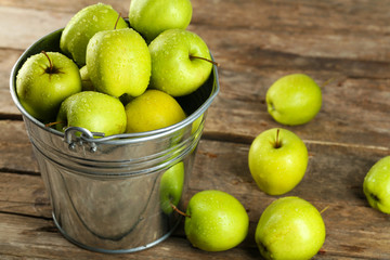 Ripe green apple in metal bucket on wooden table close up