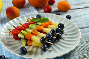 Fresh fruits on skewers in plate on table, closeup