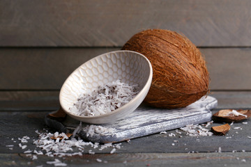 Coconut shavings in bowl with coconut on wooden background
