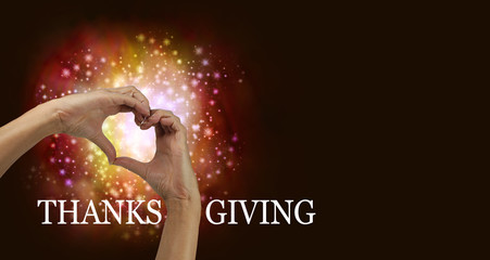 Thanksgiving Heart Hands - pair of female hands making heart shape with red orange colored sparkles behind on a dark background with copy space and the word 'THANKSGIVING' running along the bottom - obrazy, fototapety, plakaty
