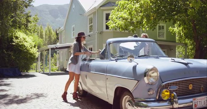 Two beautiful girl friends packing a vintage convertible car and leaving for road trip