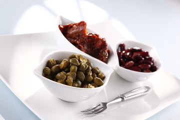 capers, tomatoes, beans in white bowls on a white background 