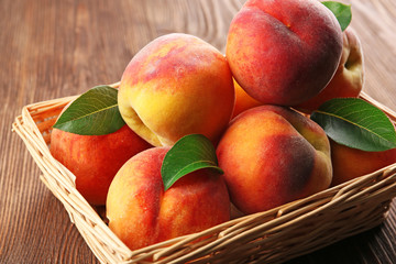 Fresh peaches in wicker basket on wooden table, closeup