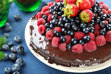 Delicious chocolate cake with summer berries on blue tablecloth, closeup