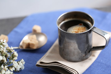 Metal cup of flavored coffee with lump sugar and flowers on table with napkin, closeup