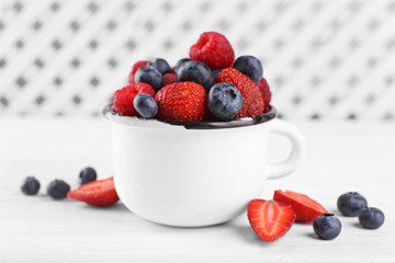 Tasty ripe berries in cup on wooden table close up