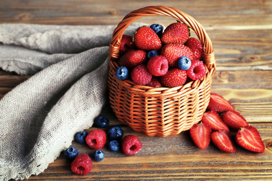 Tasty ripe berries in basket on wooden table close up