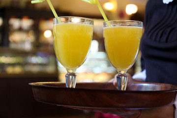 Glasses of yellow cocktails on tray in waiter hands in cafe