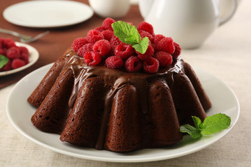 Tasty chocolate muffin with glaze and raspberries on table close up