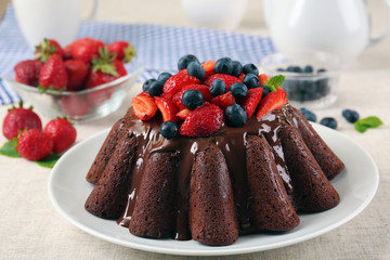Tasty chocolate muffin with glaze and berries on table close up