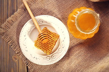 Pot of honey and honeycomb with dipper on wooden background
