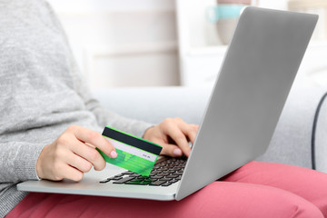 Naklejka premium Concept for Internet shopping: woman with laptop and credit card sitting on sofa, at home