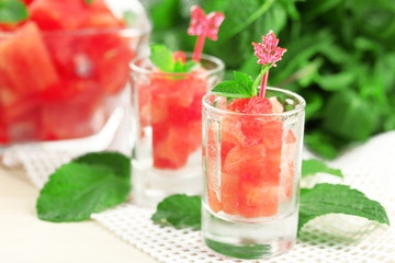 Cold watermelon pieces in glasses, on wooden table background