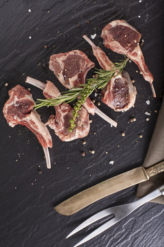 Rack of lamb, Raw rack of lamb cut in pieces decorate and seasoning with rosemary tomato herbs and olive oil fork and knife on black stone