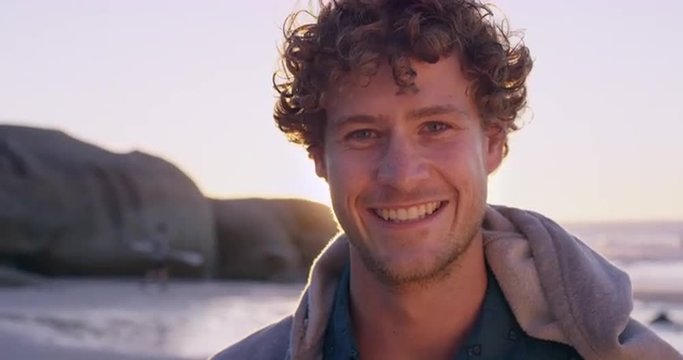 Portrait of attractive man smiling on beach at sunset in slow motion