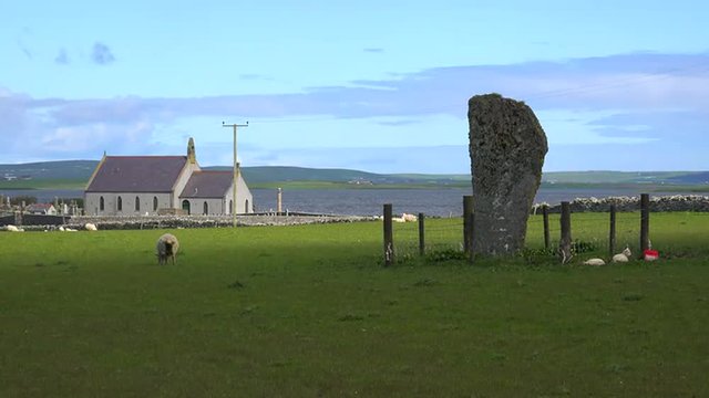 The sacred Brodgar circular Celtic stones on the Islands of Orkney in Northern Scotland with church background.