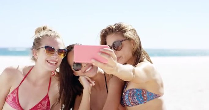 Three teenage girl friends taking selfie on beach wearing colorful bikini sharing vacation photo