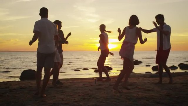 Group of Happy Young People are Dancing on the Beach in Sunset Light