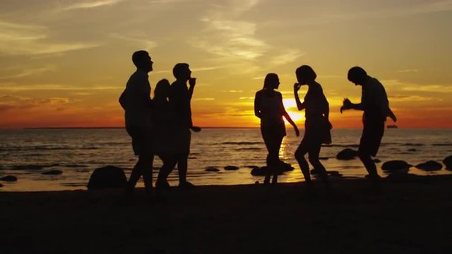 Group of Happy Young People are Dancing on the Beach in Sunset Light