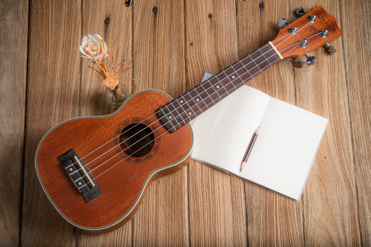 ukulele with notebook on wood background