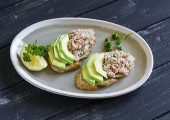 sandwich with avocado, salmon and whole wheat bread on an oval plate on a dark wooden surface, a healthy snack or Breakfast