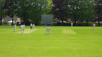The sport of cricket is played on a green grass pitch in England.