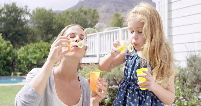 Mother and Daughter blowing bubbles in the yard happy family home