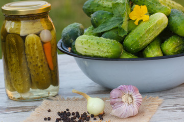 Cucumbers in metal bowl, spices for pickling and jar pickled cucumbers on table