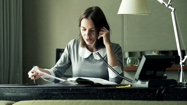 Angry businesswoman with documents and tablet talking on cellphone in office
