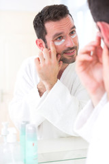 Young attractive man applying anti dark circles cream around eye