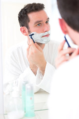 Young attractive man shaving his beard in front of a mirror