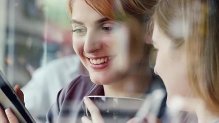 Two Women using digital tablet drinking coffee in cafe - Powered by Adobe