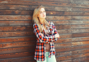 Fashion young blonde woman in checkered shirt over brown wooden