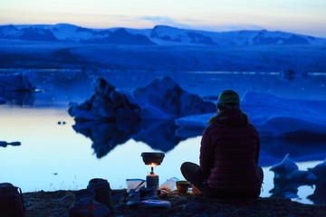 Female hiker cooking dinner at the Jokulsarlon lagoon on Iceland at dusk.