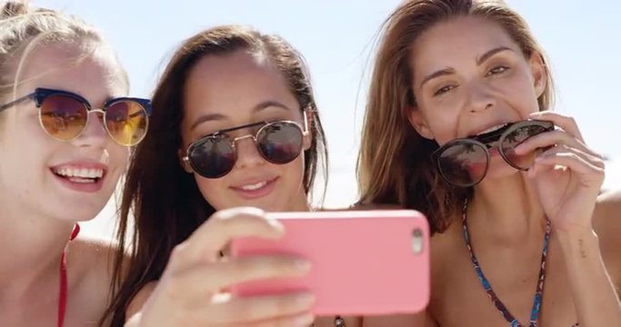 Three teenage girl friends taking selfie on beach blowing kiss pulling funny faces sharing vacation photo