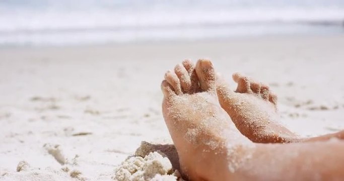 Close up of sandy feet wiggling toes two beautiful young woman sitting on tropical beach vacation