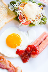 fried eggs with bacon, sausages and toasts on white plate