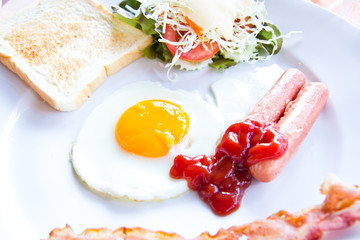 fried eggs with bacon, sausages and toasts on white plate