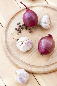 Red onion and garlic bulbs on wooden board close-up, selective focus