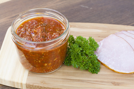 Homemade tomato sauce in glass jar with tasty ham smoked whole and sliced close-up, selective focus