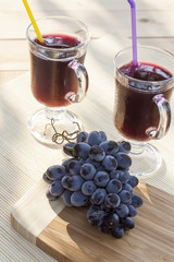 Grape juice cooler with ice in glass and glass of fresh blue grapes on a wooden table close-up, selective focus