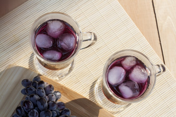 Grape juice cooler with ice in glass and glass of fresh blue grapes on a wooden table close-up, selective focus