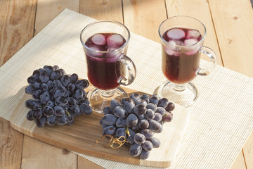 Grape juice cooler with ice in glass and glass of fresh blue grapes on a wooden table close-up, selective focus