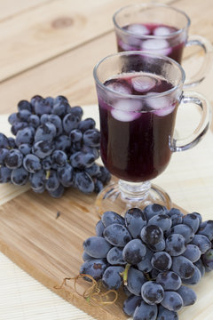 Grape juice cooler with ice in glass and glass of fresh blue grapes on a wooden table close-up, selective focus