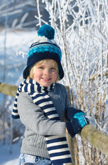 Portrait of a little smiling  boy in winter hat in the snow forest