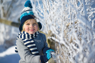 Portrait of a little smiling  boy in winter hat in the snow forest