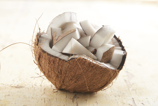 half coconut filled with coconut chunks on a wooden plank. brightly lit