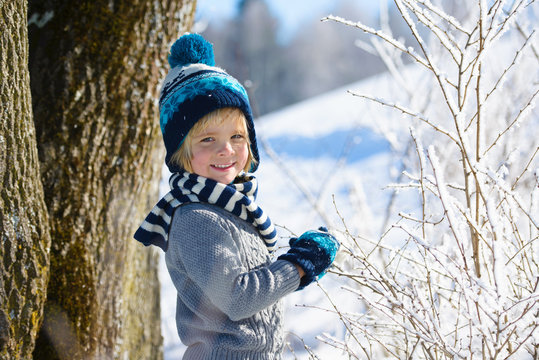 Happy little boy in winter hat in snow forest